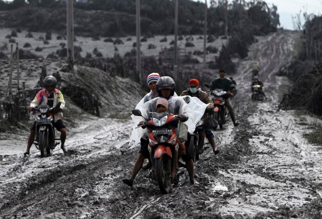 De lokale bevolking van het dorpje Sigarang-Garang vlucht uit het gebied per scooter. De weg is bedolven onder een dikke laag as. 